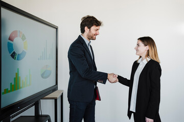 Smiling businesswoman and businessman doing hand shake in board room