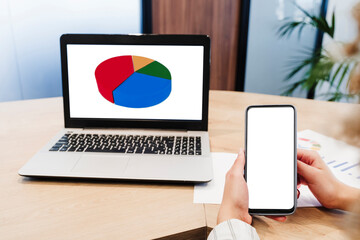 Hands of businesswoman showing blank screen of smart phone near laptop with pie chart at office