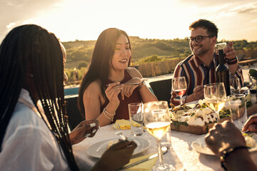 Diverse group of friends at reunion eating and drinking wine outdoor.