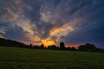 Natural Sunset Sunrise Over Field Or Meadow. Bright Dramatic Sky And Dark Ground. Countryside Landscape Under Scenic Colorful Sky At Sunset Dawn Sunrise. Sun Over Skyline, Horizon. Warm Colours.