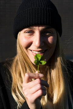 Smiling young woman holding four-leafed clover