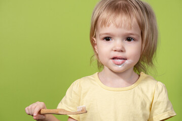 A small child brushes his teeth with an eco-friendly brush on a green background