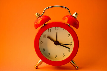 new red round clock on orange table, side view