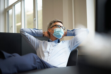 Businessman with hands behind head wearing protective face mask at office