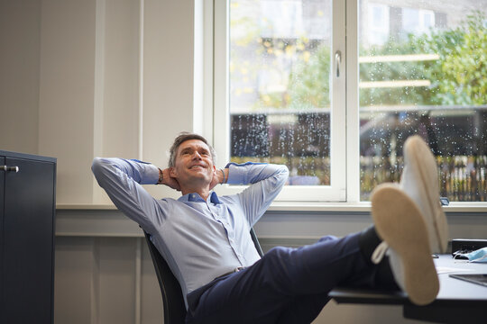 Businessman day dreaming with hands behind head at office