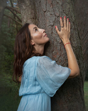 Woman in blue dress embracing tree