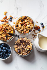 Different types of homemade granola (fruit, nut and chocolate) in jars on white kitchen table. Breakfast food concept.