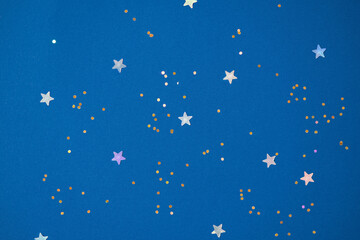 Fototapeta na wymiar Festive background with holographic sparkling stars confetti on dark blue background. Christmas, New Year or birthday party background for your project