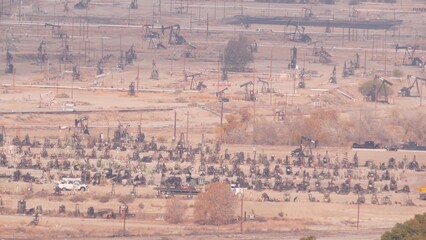 Wells with pump jacks on oil field, California USA. Rigs for crude fossil extraction working on oilfield. Industrial landscape, derricks in desert valley. Many pumpjacks platforms on oilwells pumping.