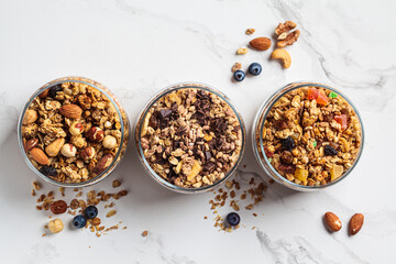Different types of homemade granola (fruit, nut and chocolate) in jars on white kitchen table. Breakfast food concept.