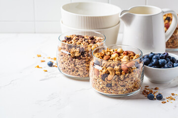 Different types of homemade granola (fruit, nut and chocolate) in jars on white kitchen table. Breakfast food concept.