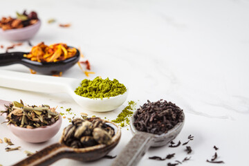 Various types of dry tea in spoons on a white marble background. Green, matcha, citrus, black and...