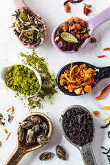 Various types of dry tea in spoons on a white marble background, top view. Green, matcha, citrus, black and herbal detox tea.