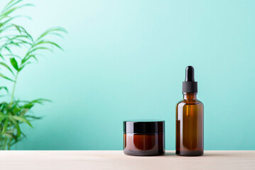 Amber glass dropper bottle and jar for cream or lotion. Skin care concept on mint and wooden surface background with green palm leaves. Spa natural cosmetic concept for face body care
