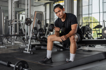Fototapeta na wymiar Asian man exercises in fitness. Young healthy man in sportwears doing arms exercise in gym.