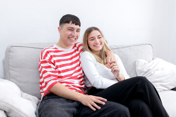 Young couple at home sitting in the sofa laughing. Heterosexual 18-20 years old couple.