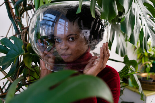 Young woman with pot over face amidst green plants at home