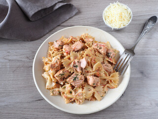Pasta farfalle with pieces of fish salmon in cream sauce with parmesan cheese in a plate, napkin, fork on a light table, flat layout. Traditional delicious dish with curly  pasta products and seafood