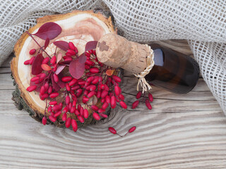 Berries and leaves of the useful berberis plant and berberis cider, syrup in a bottle, napkin on a wooden table, top view, flat layout. Seasonal red barberry fruit and drinks for use in medicine 