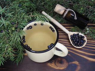 Herbal tea with juniper berries in a mug and extract of tincture in bottle on a wooden background,...