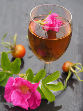 Drink in a wine glass, bright flower with leaves of wild roses, ripe wild rosehip berries on a dark wet table Beautiful picture for the wishes of good health. Vertical photo for decoration and design