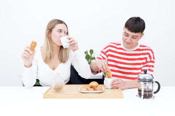 Boyfriend and girlfriend having breakfast at home, eating croissants and drinking coffee. Girl looking at his boyfriend. Young couple at home. Heterosexual 18-20 years old couple.