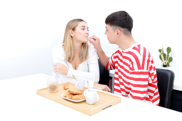 Boyfriend and girlfriend having breakfast, eating croissants and drinking coffee. Boy cleaning his girlfriend's mouth. Young couple at home. Heterosexual 18-20 years old couple.