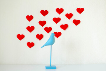 Peace and love. A statuette of a blue bird and red hearts on a white background. A gift card for Valentine's Day. The concept of sublime love. Minimal concept.