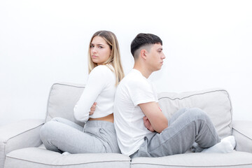 Obraz premium Angry couple sitting in the sofa back to back with crossed arms. woman looking at camera. Young couple at home. Heterosexual 18-20 years old couple.