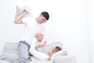 Boyfriend and girlfriend pillow fighting in the sofa. Young couple at home. Heterosexual 18-20 years old couple.