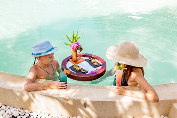 cute siblings school boy and teenage girl with served floating tray in swimming pool with drinks and snacks on tropical island resort in Maldives, cocktails and canapes in luxury hotel, travel concept