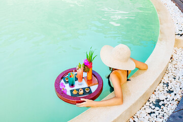 cute teenage girl with served floating tray in swimming pool with drinks and snacks on tropical...