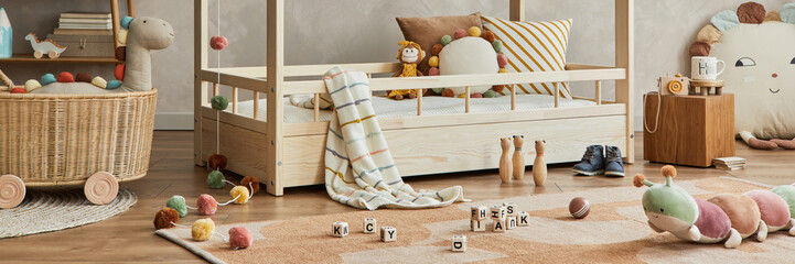 Fototapeta na wymiar Creative composition of cozy scandinavian child's room interior with wooden bed, plush and wooden toys and textile hanging decorations. Neutral creative wall, carpet on the parquet floor. Template.