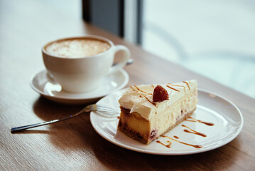 Cup of coffee and piece of raspberry cheesecake on cafe table near window, breakfast at public place