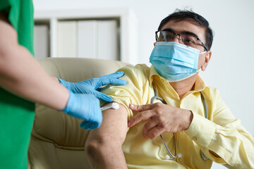 General practitioner in medical mask getting injection of vaccine against coronavirus in shoulder
