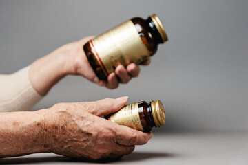 Close up of hands of senior woman holding two jars of medicine. Gray background. Concept of treatment