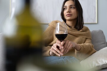 Pretty, attractive, stylish young woman sitting on couch having raised glass with red wine, examine, taste beverage