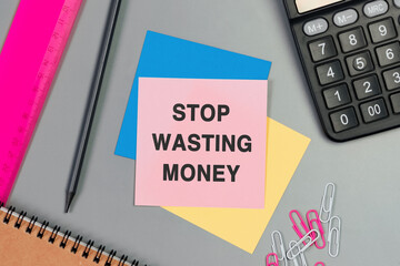 Stop Wasting Money - text on sticky note. Top view image of pink card, pencil, calculator and with many paper clips on table. Flat lay design