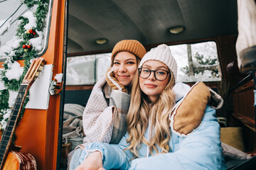 Portrait of two cheerful young women  friends sitting in a van in winter camp.