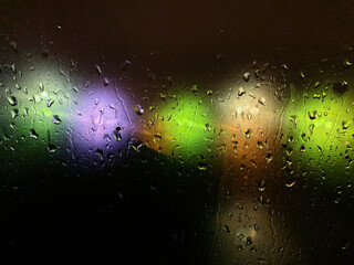 Colored blurry lights on a dark background through the drops on the glass