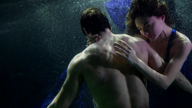 pretty woman is embracing her boyfriend underwater, loving couple is floating in water of sea