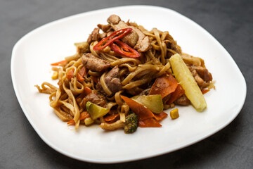 Fried noodles with sauce, meat, chili and sesame seeds on a white plate. Traditional Asian cuisine