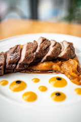 Roasted duck cut into pieces close-up with pumpkin puree on a white plate