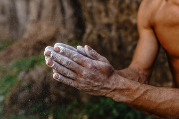 Fototapeta premium Outdoor rock climbing. The hands of a tanned athlete are smeared with magnesia powder close-up on a forest background
