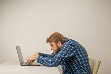 Beard emotional man in slouching position sitting in office room, working with laptop