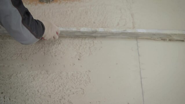 A plasterer plasters a concrete wall with a spatula. Worker aligns wall. Leveling plaster on the wall with a tool.