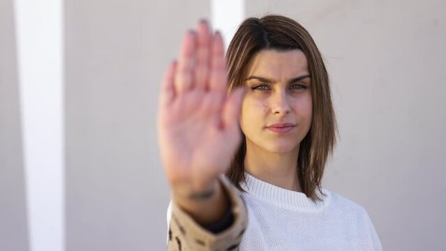 Pan right of a young woman raising her hand doing prohibition gesture