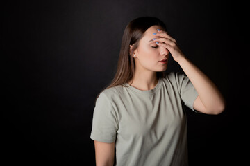 Headache. A young brunette in a T-shirt clutched her head with her hand, illness or fatigue. Portrait on a black background, copy the space on the left