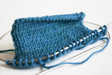 Stockinette stitch knitting on circular needles close up, blue turquoise knit stitches on white...