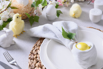 Easter table setting and dinner with yellow chick, festive decorations, fresh flowers and eggs. Close up.